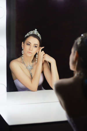 Reflection of a beautiful woman posing in a studio with a crown on her head dressed in a dress