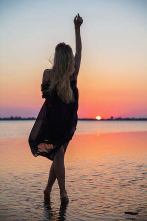Alluring silhouette of a woman wearing a dress posing against the backdrop of the sea and colorful sunsetの写真素材