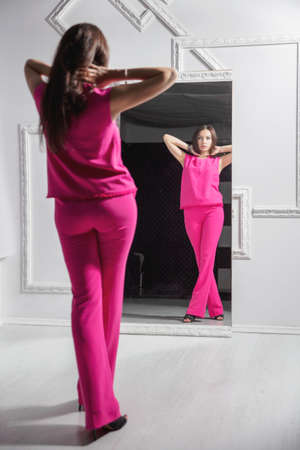 Reflection of a beautiful woman posing near the mirror in the studio, dressed in a pink suit