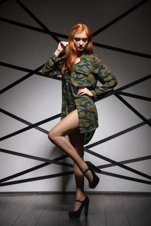 Pretty red-haired woman posing in studio wearing a khaki shirtの写真素材