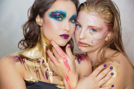 Two lovely young women with creative make-up on the face posing in the studio.の写真素材