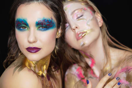 Two sexy young women with creative make-up on the face posing in the studio.の写真素材
