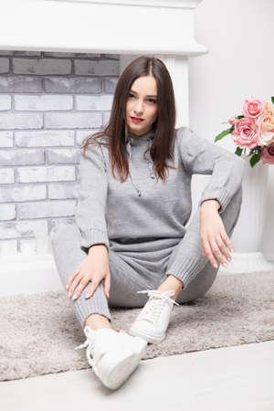 Young brunette dressed in a gray suit posing near the fireplace