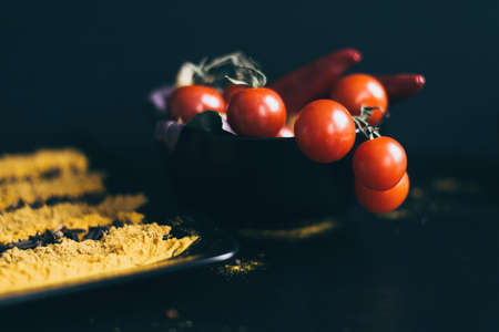 A black dish of delicious fresh tomatoes cherry lying on a wooden cutting board. Herbs and basil are used as a decoration.の写真素材