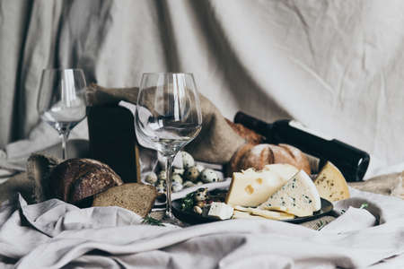 Two empty wineglasses are standing ready to be filled with dry red wine lying behind. Fresh bread, blue cheese, masdaam cheese and quail eggs are used as decoration.の写真素材
