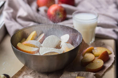 Fresh red apples sprinkled with flour in a stylish iron dish lying on a white window sill. Apple slices and a glass of milk are used as decoration.の写真素材