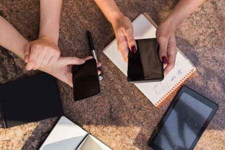 close up of girls hands holding phones. there are notebooks and pens around. good shotの写真素材