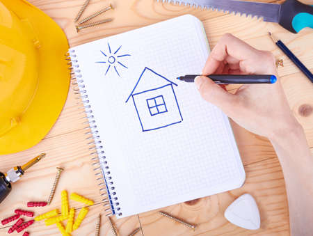Hand drawing a house and different tools  on a wooden background の写真素材