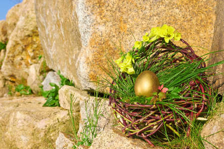 Gold easter egg in brown basket on a rockの写真素材