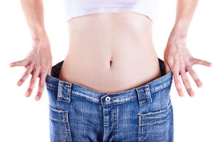Slim woman shows her weight loss by wearing an jeans, isolated on white backgroundの写真素材