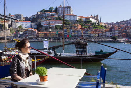 Young woman sitting in a cafe on the banks of the River Douru, Porto, Portugalの写真素材