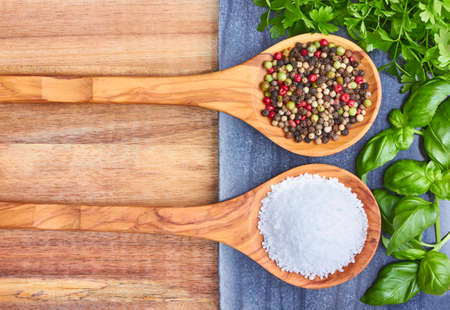 Sea salt, peppercorns and basil, parsley on wooden spoonsの写真素材