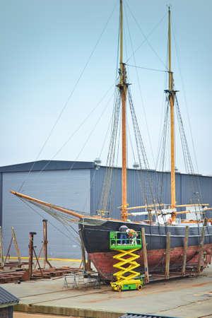 Sail boat with workers in a boatyard being repaired and restored