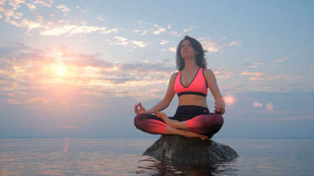 Yoga woman in lotus pose on rock in sea water at sunriseの写真素材