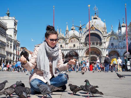 Beautiful young woman feeding pigeons on the Piazza San Marcoの写真素材