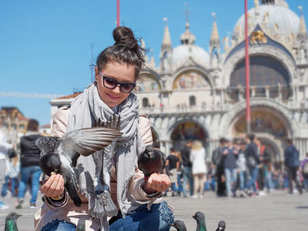 Young female traveler sitting and feeding pigeons on the Piazza San Marcoの写真素材
