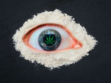 Drug abuse concept, overdose human eye with a leaf of marijuana in the pupil and heroin powder aroundの写真素材