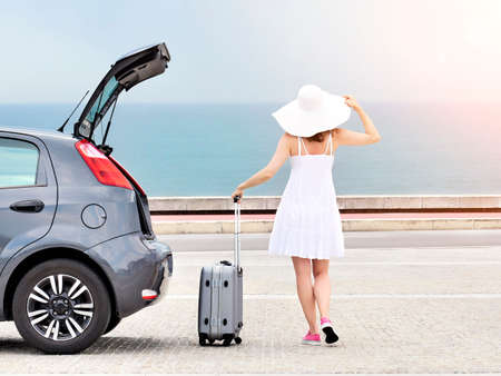 Woman with travel bag standing near hatchback car, Back viewの写真素材