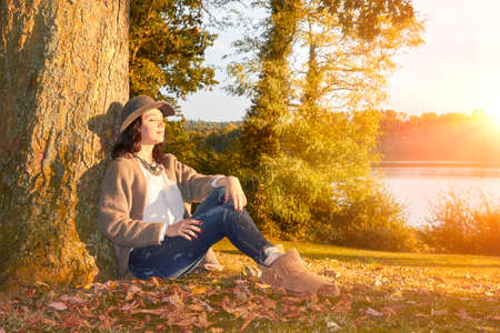 Woman sitting leaning on tree in fall parkの写真素材