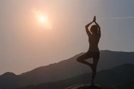 Woman silhouette practicing yoga, mountains and sky backgroundの写真素材