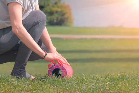 Woman going to practicing yoga, unrolling or rolling her yoga mat on green grassの写真素材