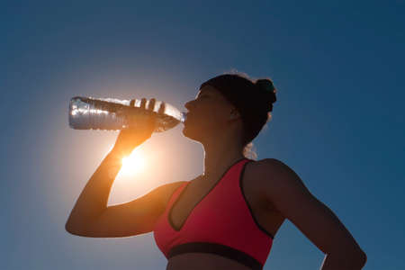 Sport woman drinking water from bottle against the sunの写真素材