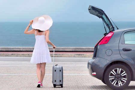 Woman with travel bag standing back near hatchback carの写真素材