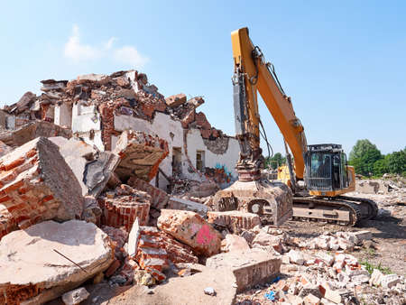 Excavator working in rubble at sunny day. Old building ruins view.の写真素材