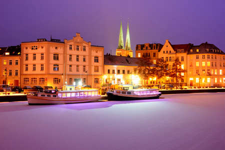 Boats on Frozen Trave river at nights. Lights on Lubeck city embの写真素材