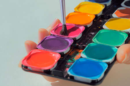 Female hands holding art palette with paints and paintbrushの写真素材