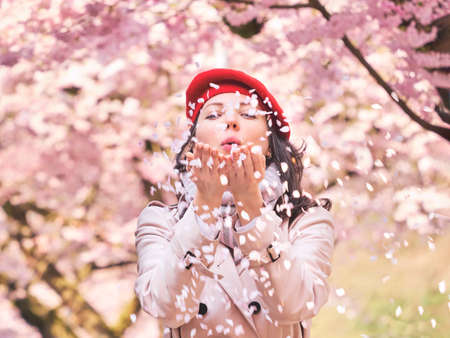 Beautiful Woman blowing petals in her hands, enjoying a flowering spring gardenの写真素材