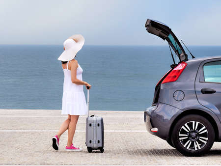 Woman tourist with travel bag standing near hatchback carの写真素材