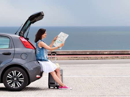 Woman traveler on hatchback car on seaside road.の写真素材
