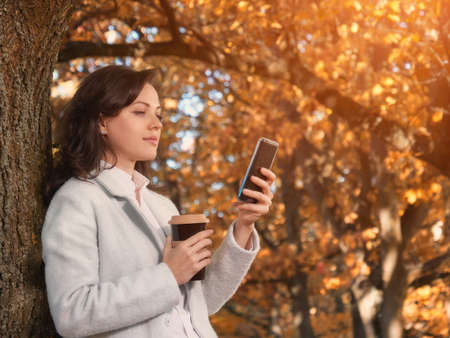 Beautiful woman drinking coffee outdoor and chatting on smartphoneの写真素材