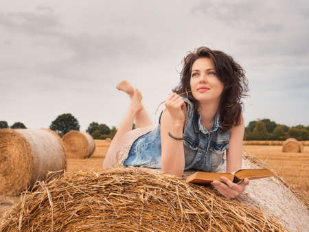 Beautiful Woman Reading book on a haystack, nature backgroundの写真素材