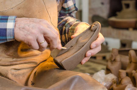 Old hands of a potter shaping a clay figure
