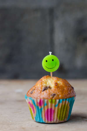 Homemade chocolate chip cupcake and candle smiling. Rustic background.の写真素材