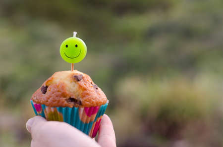 Homemade chocolate chip cupcake and candle smiling in the hand of a child.の写真素材