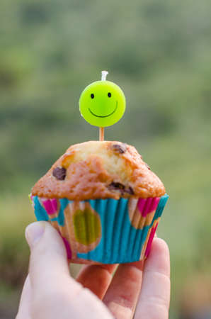 Homemade chocolate chip cupcake and candle smiling in the hand of a child.の写真素材
