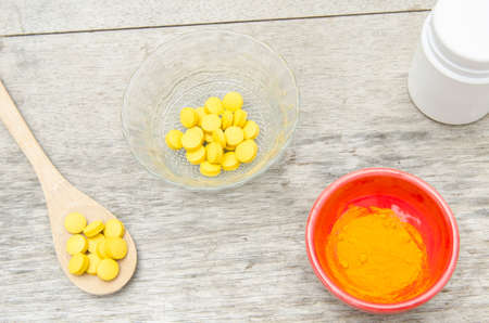 Turmeric herbal tablets in white bottle ,fresh turmeric powder in wooden spoon on wooden backgroundの写真素材