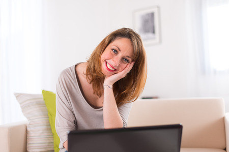 cheerful young women at home working on her laptop computerの写真素材