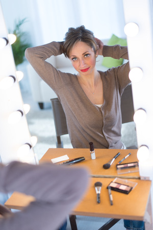 cheerful young women adjusting her make-up in a make-up mirror の写真素材