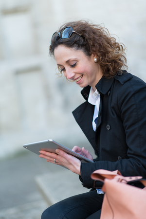 portrait of a beautiful young woman outside playing with tablet computerの写真素材