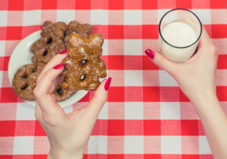 Top view on woman's hands holding cookie and glass of milk over  checkered tableclothの写真素材