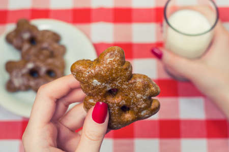 Close up photo of woman's hands holding cookie and glass of milk over checkered tableclothの写真素材