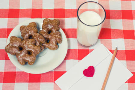 Top view of plate with cookies glass of milk and envelope with a love letter inside on checkered tableclothの写真素材