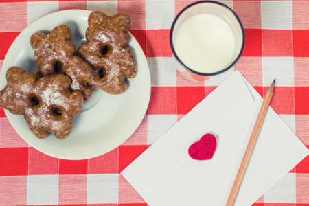 Close up photo of tasty biscuits glass of milk and envelope with love letter inside on checkered backgroundの写真素材