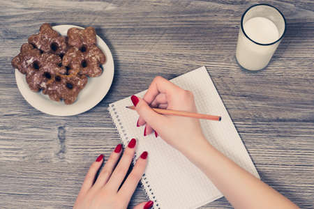 Top view on woman's hands writing essay in notepad and having a snackの写真素材