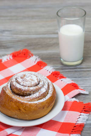 Vertical photo of appetite cinnamon roll on chechered tablecloth and glass of milkの写真素材