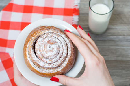 Top view of woman's hand holding a cinnamon roll with powdered sugar on white plateの写真素材